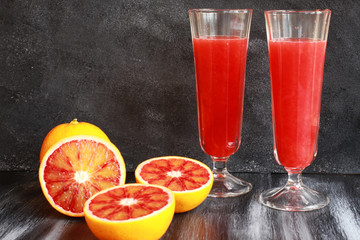 Orange juice with cut blood oranges on dark board