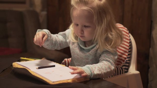 Little girl baby blonde draws with pencil.