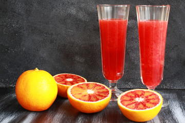 Orange juice with cut blood oranges on dark board