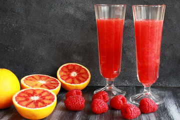 Orange juice, blood orange and raspberries on dark board