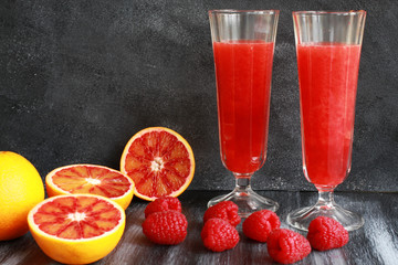 Orange juice, blood orange and raspberries on dark board