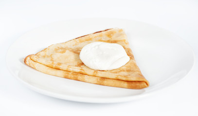 Thin delicious pancake with sour cream on white