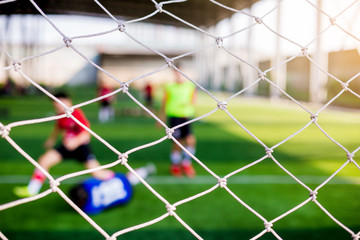 Mesh of goal with blurry of soccer goalkeeper and soccer players