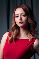 Fototapeta premium Charming brunette in a red dress posing on a black background.