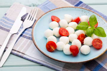 Delicious caprese salad with ripe cherry tomatoes and mini mozzarella cheese balls with fresh basil leaves.