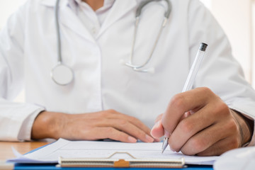 Healthcare medical Expenses concept, Hands Doctor's writing and working on prescription clipboard with record information paper folders on desk in hospital or clinic. Selective focus