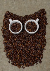 Owl made from coffee beans. Whole bean coffee. Coffee beans in the shape of an owl. Coffee cup on coffee beans. Coffee beans on burlap