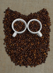 Owl made from coffee beans. Whole bean coffee. Coffee beans in the shape of an owl. Coffee cup on coffee beans. Coffee beans on burlap