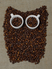 Owl made from coffee beans. Whole bean coffee. Coffee beans in the shape of an owl. Coffee cup on coffee beans. Coffee beans on burlap