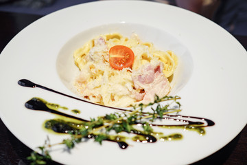 White deep plate with portion of pasta with meat and cherry tomato garnished with sauce and herb
