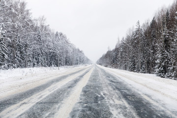Fototapeta na wymiar winter road with ice on the asphalt, trees under snow during the winter frost in Russia