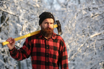 Bearded man with a hatchet, forestry. Handsome man, hipster in snowy forest. Lumberjack in the woods with an ax on winter day. Male holds an ax on a shoulder. Brutal bearded man. Male with an ax.