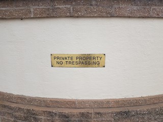 gold or brass private property no trespassing sign on wall with bricks