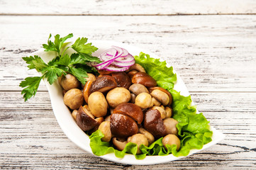 Fermented food on a white plate. Marinated mushrooms champignons with onion rings and parsley close up and copy space