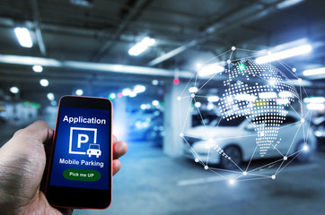 Pick me up, mobile smart phone in hand using application for intelligent car park with digital hologram on blurred parking car background, mobile auto parking, network and online technology concept - obrazy, fototapety, plakaty