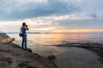 Alone artist on wooden sea bridge. Photographer with mirror camera and tripod at end of pier board. The tourists set up a camera on a wooden bridge.Fall foggy misty sunrise above smooth sea. 