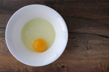 raw egg without shell in a white plate on a wooden board background