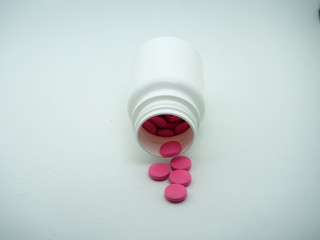 Red tablets are poured from a white plastic jar.