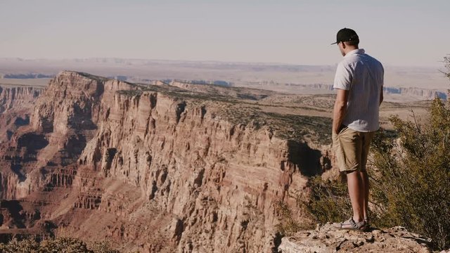 Happy successful young tourist man watching epic scenery over Grand Canyon mountains, wide cinematic background shot.