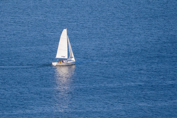 Fototapeta premium A small white sailing ship on the blue water with reflection (copy space)