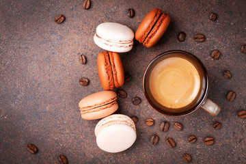 Cup of coffee and cake macaron or macaroon on brown table top view. Delicious breakfast.