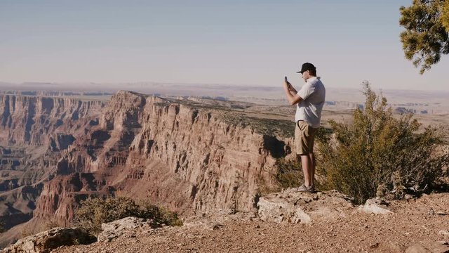 Happy young tourist man taking smartphone photo of epic summer scenery standing over incredible Grand Canyon USA.