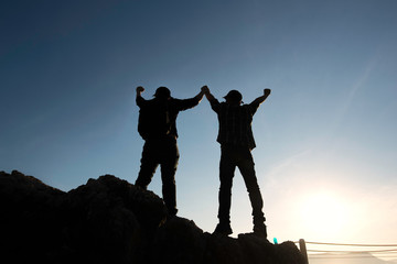 Asia couple hiking help each other silhouette in mountains with sunlight.Silhouette man lifts his hand on a rocky seashore. 