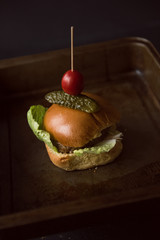 A beautiful brioche burger bun , with an organic beef burger, lettuce, gherkin and tomato. Served in a rustic metallic tray, photographed in a dark setting. Hipster food.