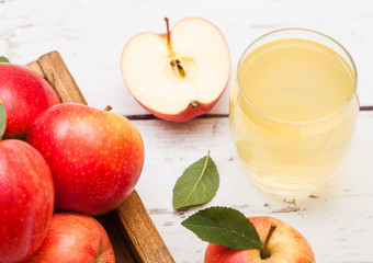 Glass of fresh organic apple juice with red apples in vintage box on wooden background