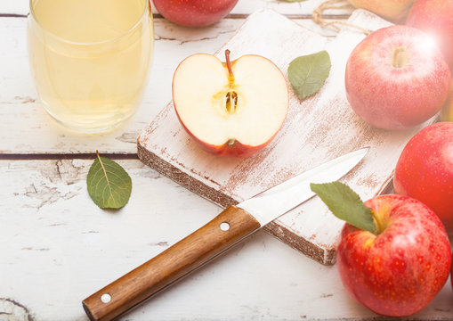 Glass of fresh organic apple juice with pink lady red apples on chopping board on wooden background with knife