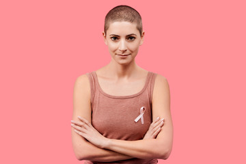 Smiling mid 30s woman, a cancer survivor, wearing pink breast cancer awareness ribbon, isolated over living coral background. Support, solidarity, screening and prevention concept. - Powered by Adobe