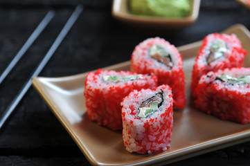 Roll Hayashi with cucumber, cream cheese, salmon and masago caviar. In the frame of chopsticks and wasabi. Black wooden background. Close-up. Macro shooting.