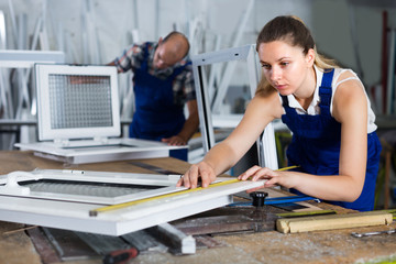 Workwoman is checking dimensions of finished plastic window usin
