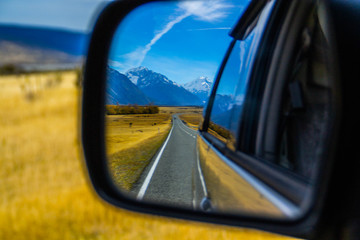Fototapeta premium Roadtrip/car traveling concept. View of back car mirror with mountain and road scenery. Aoraki/Mount Cook National Park, South Island of New Zealand.