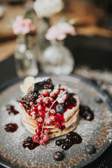 Traditional homemade dish for Pancake Day, shrove Tuesday. Stack of pancakes with blueberries, cranberries, blackberries and jam, covered in icing sugar. 