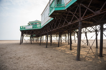 A beautiful old vintage steel iron victorian seaside pier structure shot from beneath, victorian architecture on the sandy beach, seaside landmark buildings.