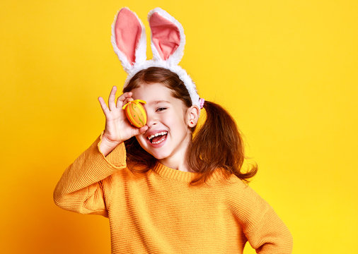 funny happy child girl with easter eggs and bunny ears on yellow