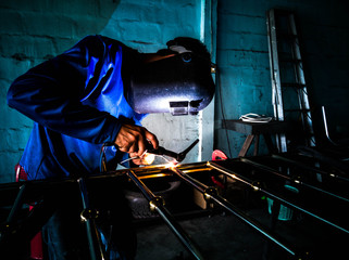 Picture of mechanic welding aluminum door with electric welding machine.