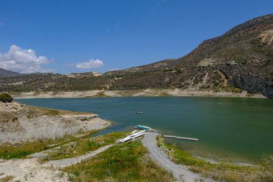 View of the germasogeia dam in Cyprus, taken on a bright blue sky day. Shot shows a path leading to canoes at the side of the vividly blue green lake.