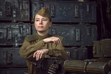 Woman soldier dressed in military uniform sitting next to a machine gun