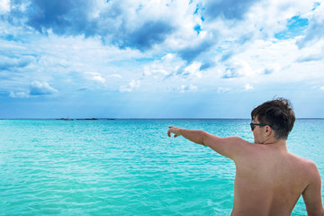 Young attractive man shows by finger to something on turquoise ocean