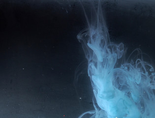 A drop of paint dissolves in water. On black background.