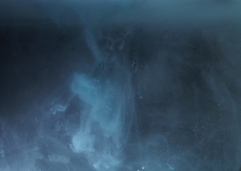 A drop of paint dissolves in water. On black background.