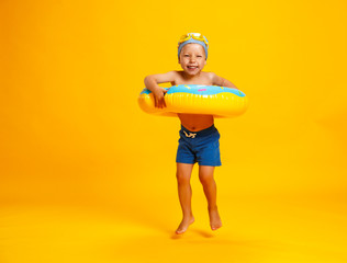 happy child boy in swimsuit with swimming ring donut on colored yellow background