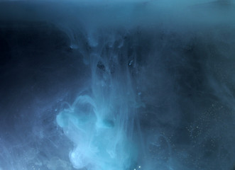 A drop of paint dissolves in water. On black background.