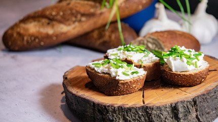 French Baguette with white curd spread decorated with green fresh chive served on wooden plate
