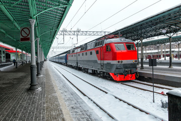 Fototapeta premium Lokomotywa elektryczna i pociąg pasażerski na kolei w mroźny śnieżny zimowy dzień.