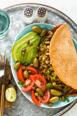 vegan breakfast of gluten-free egg-free chickpea omelet with fried mushrooms and leek. and a salad of fresh ripe tomatoes, avocados, olives and capers. healthy food for the whole family, party 