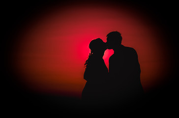 Silhouette photo of a young couple kissing at sunset on their wedding day - Red background