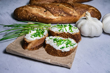 Pieces of French baguette with fresh green chives, white curd spread placed on rustic paper